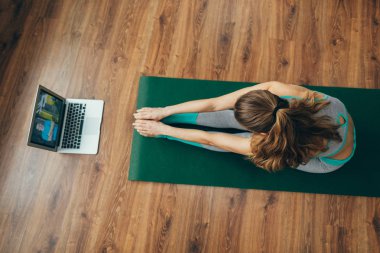 Paschimottanasana yoga pozunda oturan genç bayan.