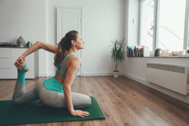 Yoga pozunda tek bacaklı genç bir kadın oturuyor.