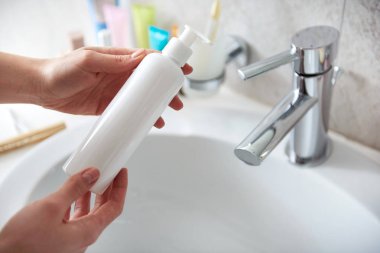 Young lady holding body lotion bottle in hand