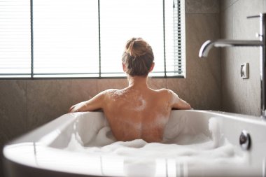 Genç ve güzel bayan evde köpük banyosu yapıyor.