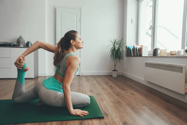 Mujer joven sentada en una pierna en pose de yoga — Foto de Stock