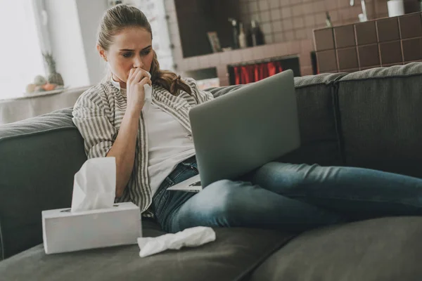 Mujer joven con frío sentado en el sofá con ordenador portátil — Foto de Stock