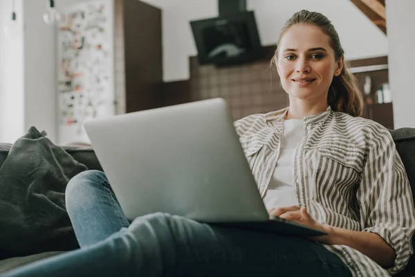Unga leende kvinna som arbetar på laptop hemma — Stockfoto