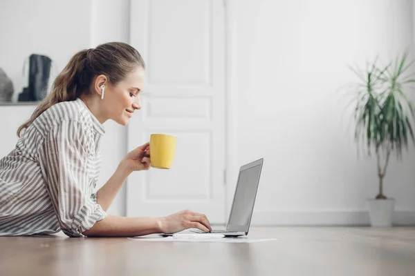 Young smiling female laying on floor with laptop — ストック写真