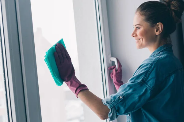 Jong glimlachend vrouw in handschoenen wassen venster — Stockfoto