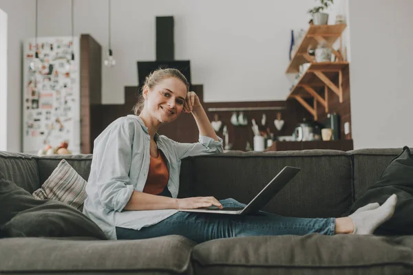 Mujer sonriente sentada en un sofá con portátil — Foto de Stock