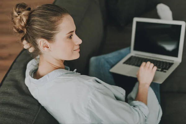 Mulher relaxada no sofá com laptop nos joelhos — Fotografia de Stock