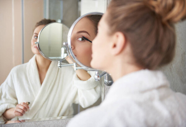 Back side of young lady putting on mascara