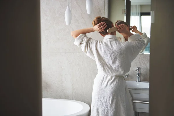 Young lady combing her hair before mirror — 스톡 사진