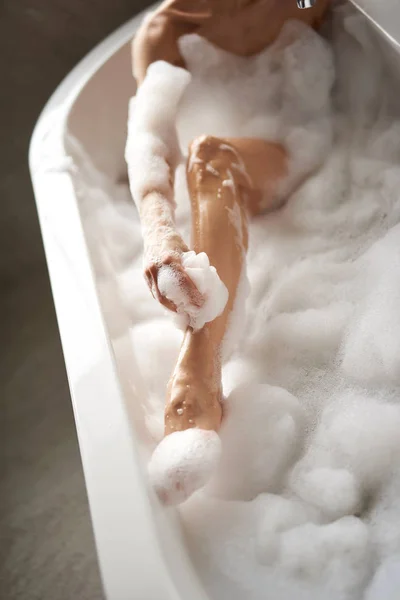 Young lady washing legs by pouf with foam — Stock Photo, Image