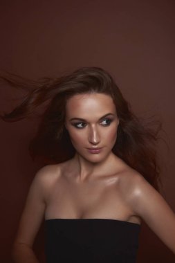 Kahverengi arka plan aleyhine poz uzun uçan saçlı çekici bayan