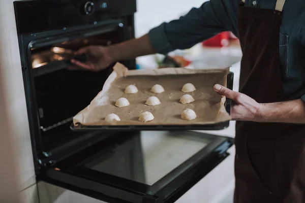 Persona sosteniendo la bandeja de hoja y poniéndola en el horno — Foto de Stock