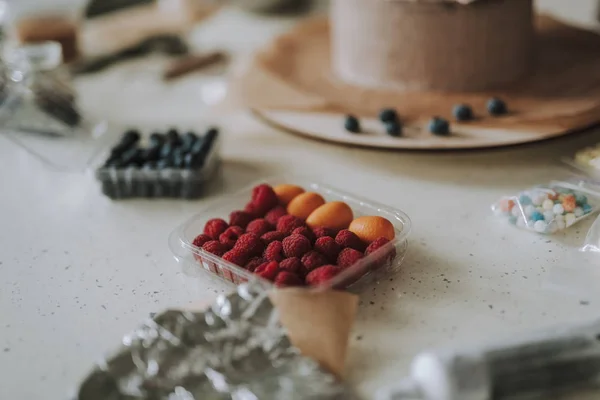 Close up of raspberries in plastic box with cake on the background