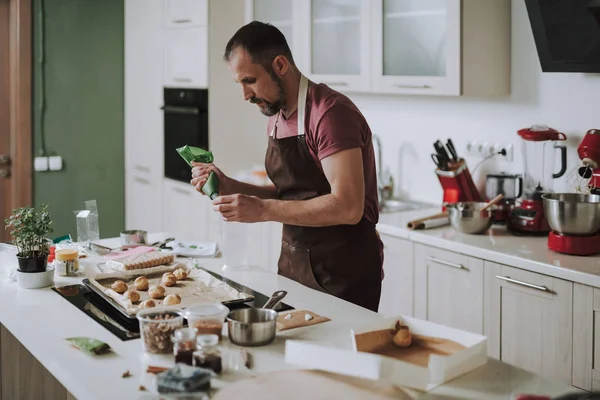 Hombre tranquilo de pie frente a la mesa de la cocina y poner crema en la pastelería — Foto de Stock