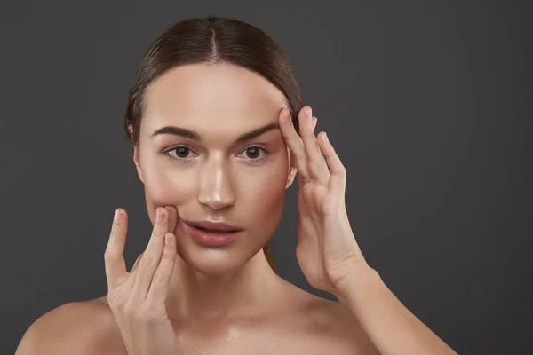Mooie jonge vrouw met natuurlijke make-up die haar gezicht aanraakt — Stockfoto