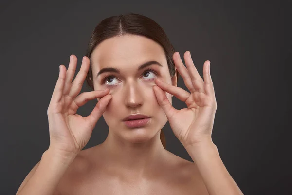 Mooie jonge vrouw die de huid onder haar ogen trekt — Stockfoto