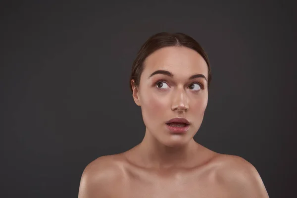 Verbaasd mooi meisje met natuurlijke make-up staande tegen grijze achtergrond — Stockfoto