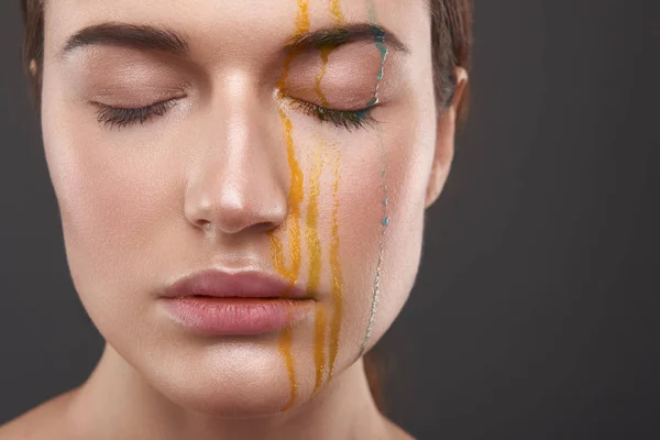 宁静的年轻女士与橙色和蓝色的液体从她的脸滴 — 图库照片