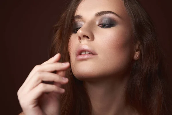Atractiva joven mujer con ojos ahumados maquillaje mirando sus dedos —  Fotos de Stock