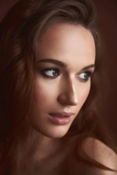 Hinreißende junge Frau mit Smoke Eyes Make-up posiert vor braunem Hintergrund — Stockfoto