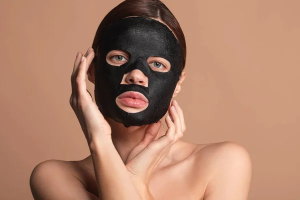 Hübsche Dame berührt ihr Gesicht, während sie eine schwarze Maske trägt — Stockfoto