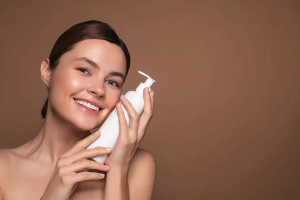 Mujer positiva presionando botella de plástico blanco en su cara y sonriendo —  Fotos de Stock