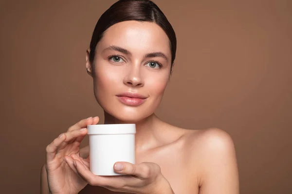 Mujer joven calma mostrando su nuevo frasco de crema facial —  Fotos de Stock