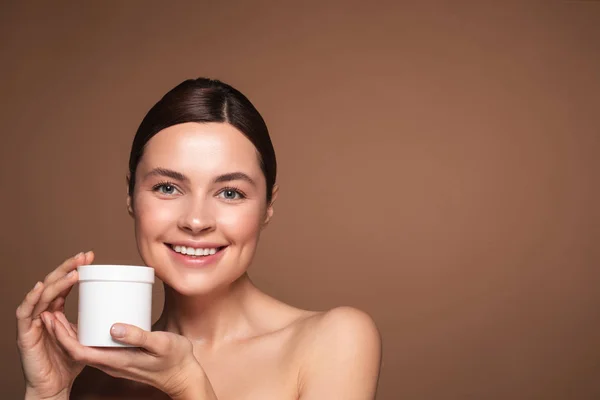 Mujer emocional de pie con crema facial y sonriente — Foto de Stock