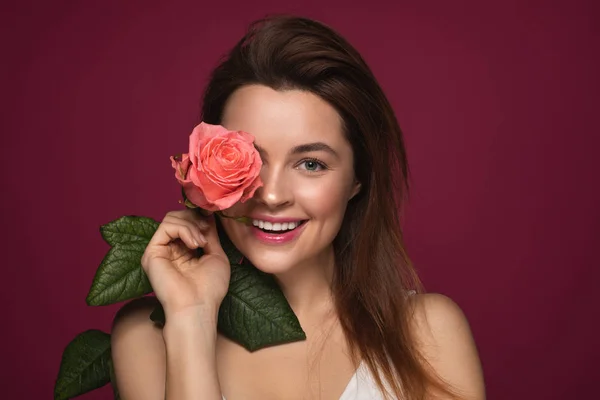 Довгошерста жінка посміхається, стоячи з рожевою трояндою — стокове фото