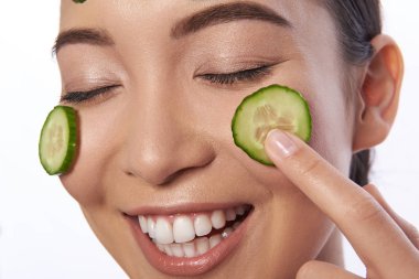 Yanaklarına salatalık dilimleri koyarken gülen pozitif kadın