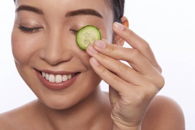 Gülümseyen ve gözüne salatalık dilimi süren bir kadın.