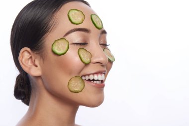 Yüzünde taze salatalık dilimleri olan bir kadın gülüyor.