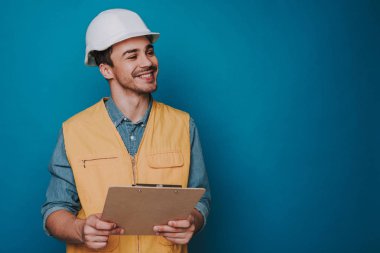 Mavi arka planda kask ve yelek giyen mutlu adam kadar bel