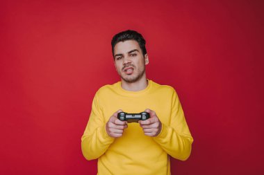 Kırmızı arka plan üzerinde joystick tutan hoş olmayan kahverengi saçlı adam yarım uzunluğu