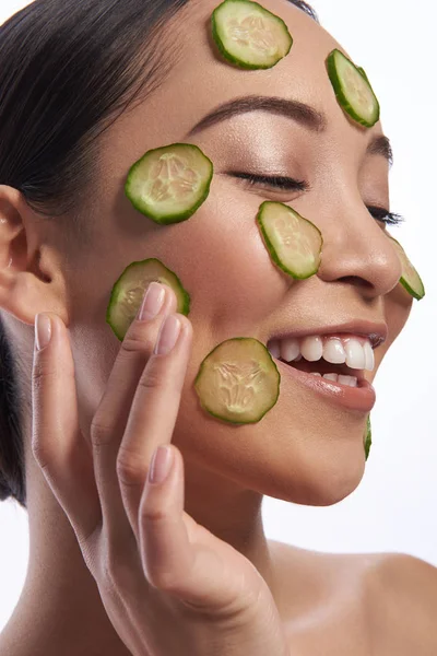 Señora feliz con maquillaje tocando rodaja de pepino en su mejilla — Foto de Stock