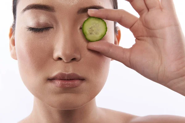 Woman closing eyes and putting cucumber slice on eyelid — 스톡 사진