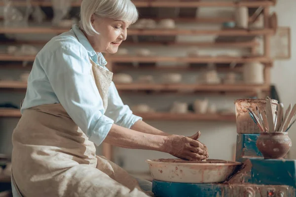 Вид сбоку на спокойную пожилую ремесленницу, работающую с глиной в мастерской гончаров — стоковое фото