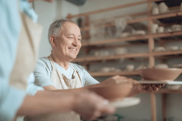 Niederer Winkel glücklicher Handwerker, der in der Werkstatt auf seine Keramikschale blickt — Stockfoto