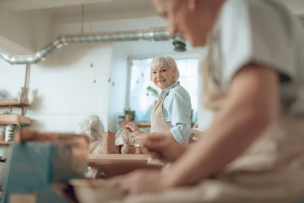 Hüftschwung einer glücklichen älteren Handwerkerin, die im Töpferatelier Steingut bemalt — Stockfoto