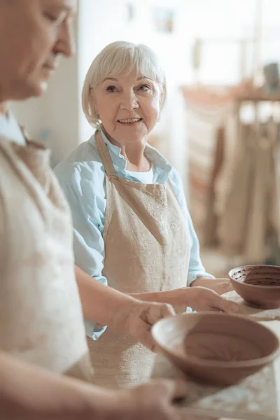 Cintura hacia arriba de alfarera femenina mirando maestro de arcilla en el taller — Foto de Stock