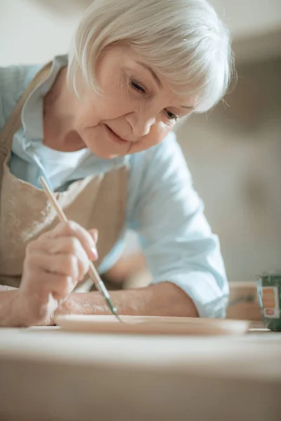 Foto recortada de anciana artesana pintando plato decorativo en taller — Foto de Stock