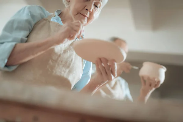 Ángulo bajo de anciana artesana pintando placa decorativa en taller — Foto de Stock