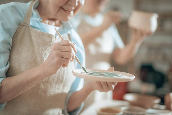 Cropped photo of elderly craftswoman painting decorative plate in workshop — Stock Photo, Image