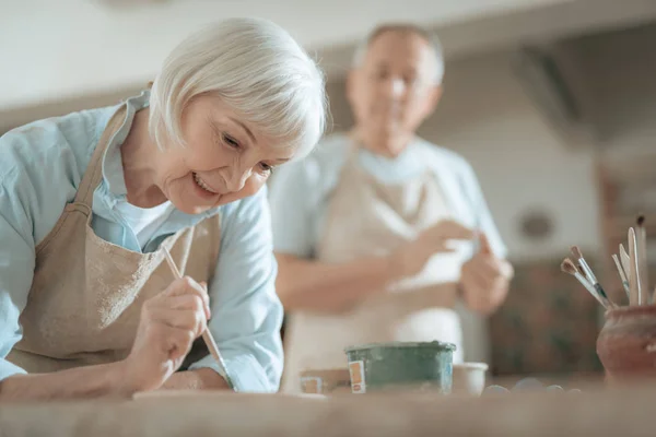 Bijgesneden foto van oudere craftswoman schilderij decoratieve plaat in workshop — Stockfoto