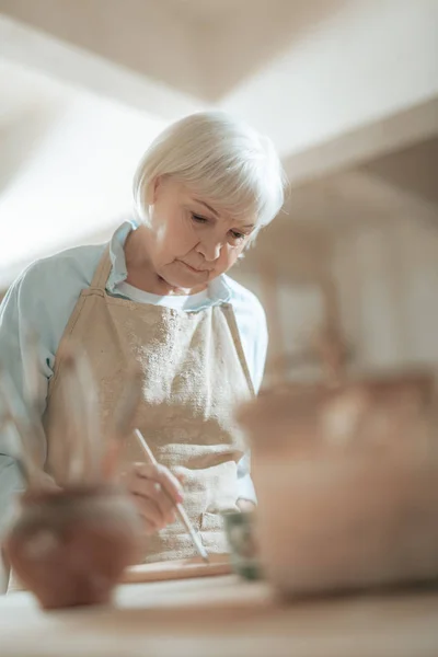 Cropped photo of elderly craftswoman painting decorative plate in workshop — Stock Photo, Image