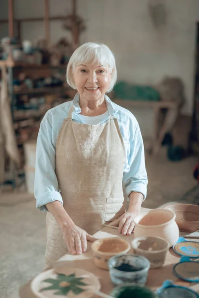 Waist up of smiling old craftswoman looking at camera in workshop — Stock Photo, Image