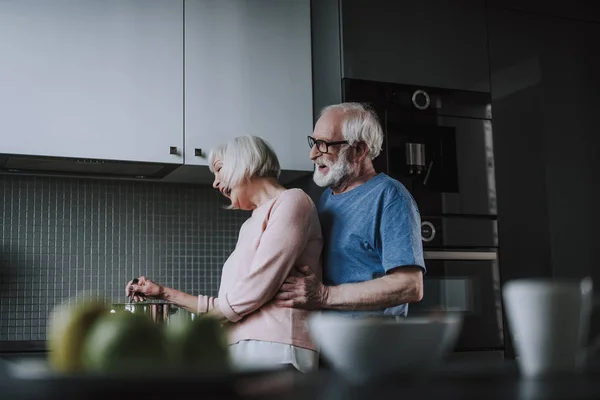Счастливая пожилая пара готовит дома на кухне — стоковое фото
