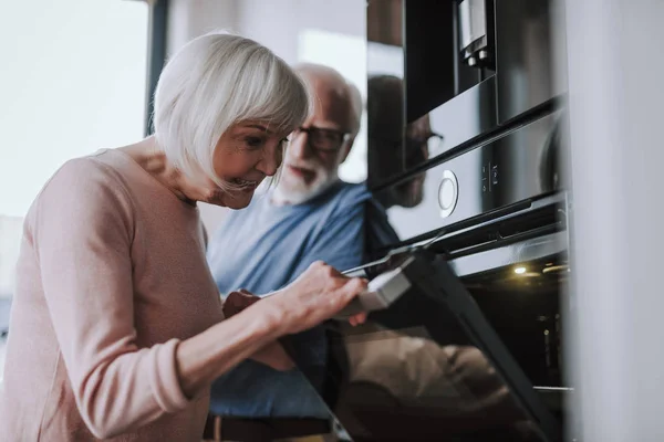 Glückliche Seniorin kocht etwas im Ofen — Stockfoto