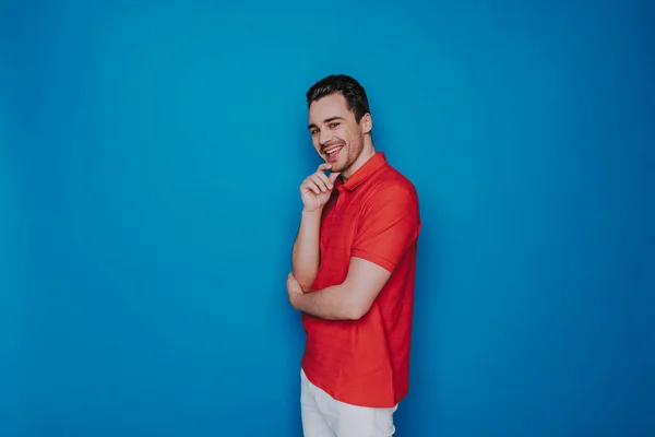 Happy Caucasian man touching chin and looking at camera on blue background — Stock Photo, Image