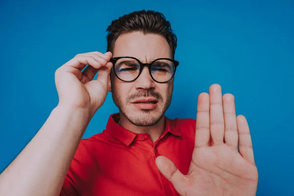 Bajo ángulo de chico caucásico en gafas entrecerrando los ojos sobre fondo azul — Foto de Stock